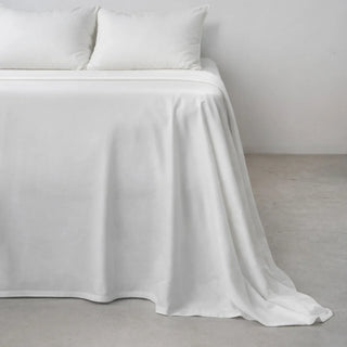 A neatly made bed dressed in clean white eucalyptus lyocell sheets in a calm, minimal room with soft daylight