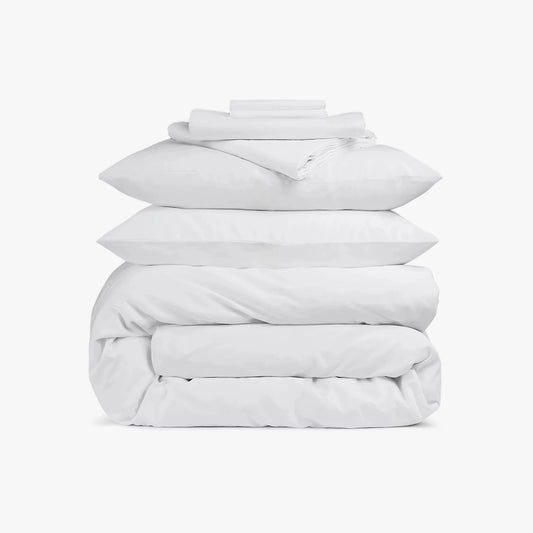 Stack of white bedding including a duvet and pillows on a white background