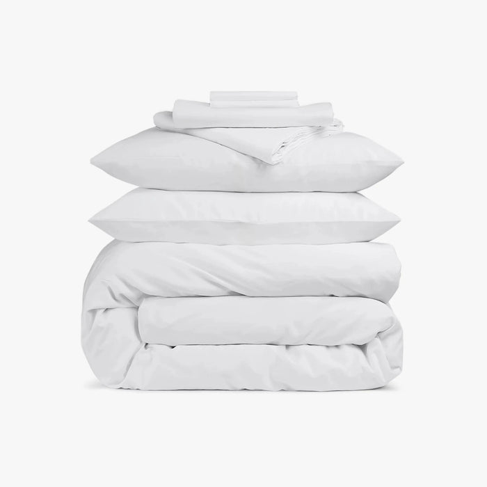 Stack of white bedding including a duvet and pillows on a white background