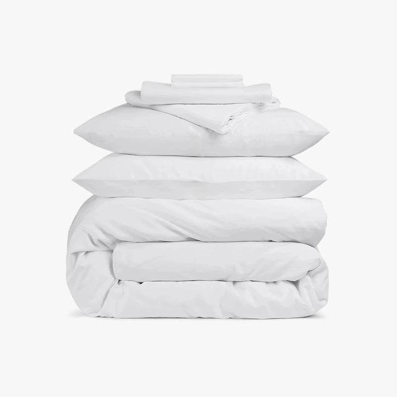 Stack of white bedding including a duvet and pillows on a white background